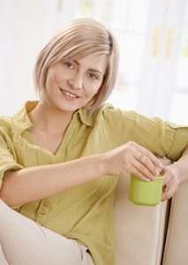 A smiling woman with short blonde hair wearing a light green shirt and holding a light green coffee cup